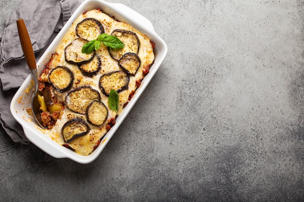 Plato mediterráneo griego Moussaka con berenjenas al horno, carne molida en cazuela de cerámica blanca sobre fondo de piedra rústica desde arriba, plato tradicional de Grecia, espacio para texto