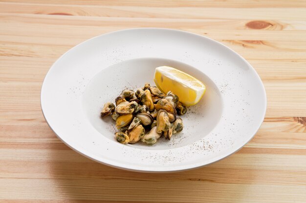 Plato con mejillones marinados y rodaja de limón sobre la mesa de madera