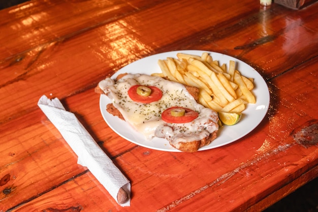 Un plato de milanesa napolitana con patatas fritas en una mesa de madera