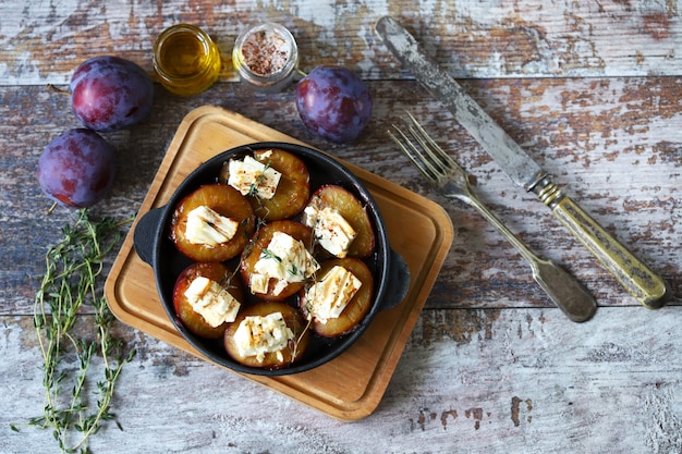 Plato con mitades de ciruela al horno con queso feta y hierbas sobre una superficie de madera en mal estado