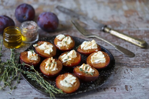 Plato con mitades de ciruela al horno con queso feta y hierbas sobre una superficie de madera en mal estado