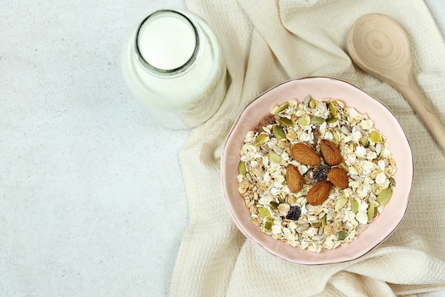 Plato con muesli, botella de leche y cuchara de madera en gris