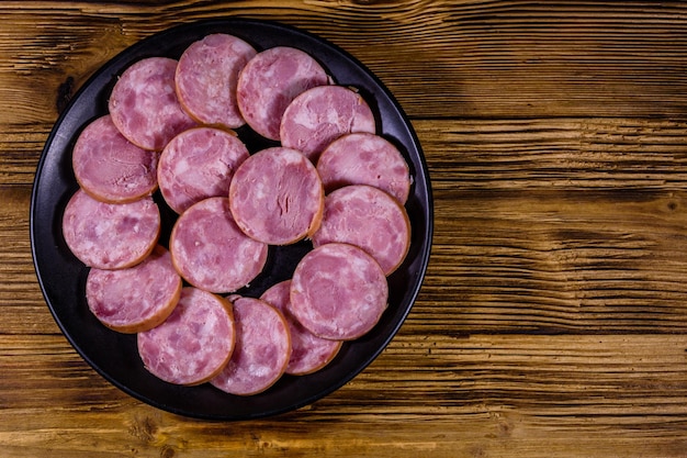 Plato negro con salchicha en rodajas sobre una mesa de madera Vista superior