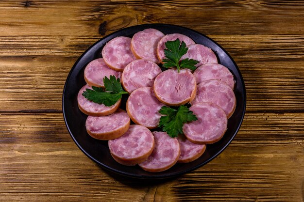 Plato negro con salchicha en rodajas sobre una mesa de madera