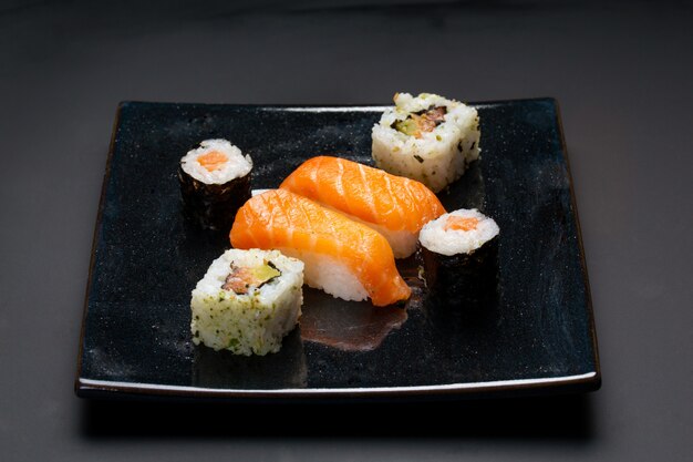 Plato negro con sushi, maki y rollos americanos