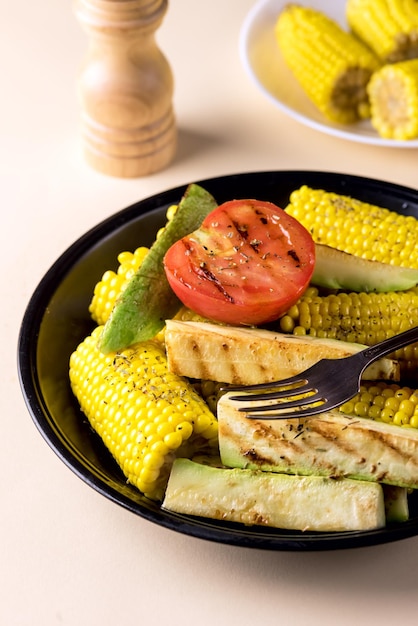 Plato negro de verduras a la parrilla Calabacín CornTomato Dieta sabrosa y saludable Comida Fondo amarillo