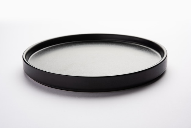Plato o bandeja redonda de cerámica negra vacía aislada en la superficie blanca