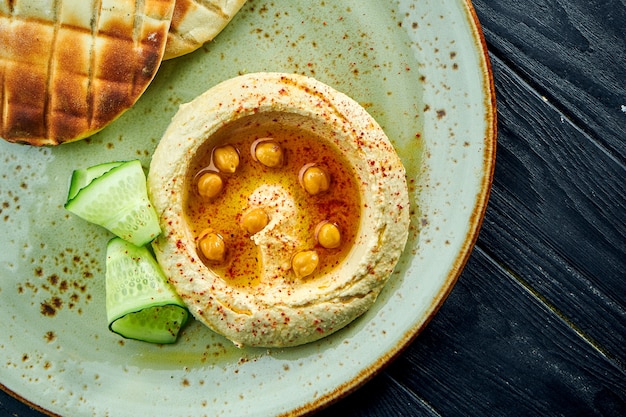 Un plato oriental clásico: hummus con aceite de oliva y garbanzos servido con pita horneada en un plato sobre una superficie de madera oscura. Comida vegetariana. Dieta