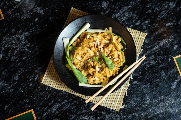 Un plato de pad thai con un menú chino al lado.