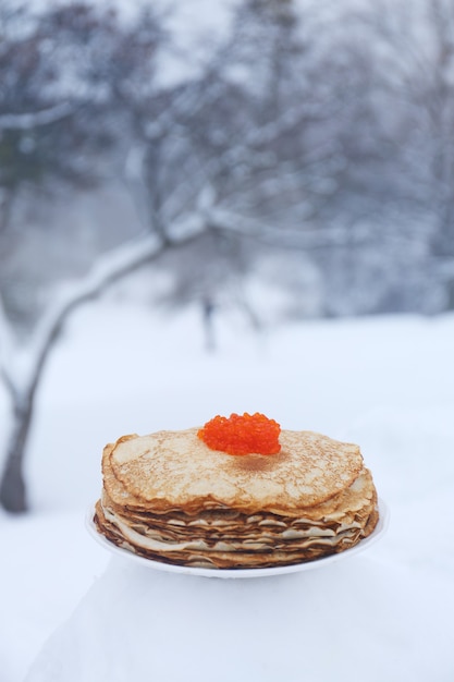 Plato con panqueques rojizos y caviar rojo sobre un fondo de paisaje invernal.