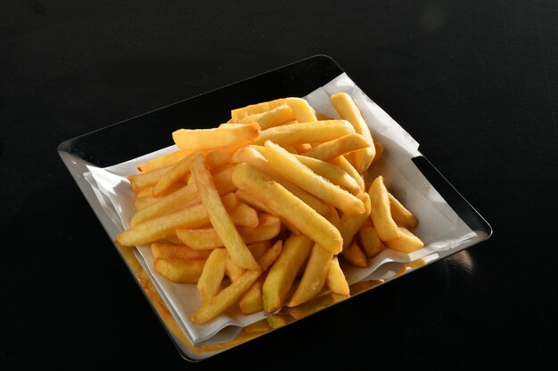 Un plato de papas fritas está sobre una mesa negra.