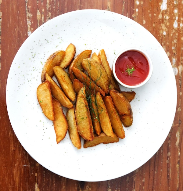 Un plato de papas fritas con una taza de ketchup encima