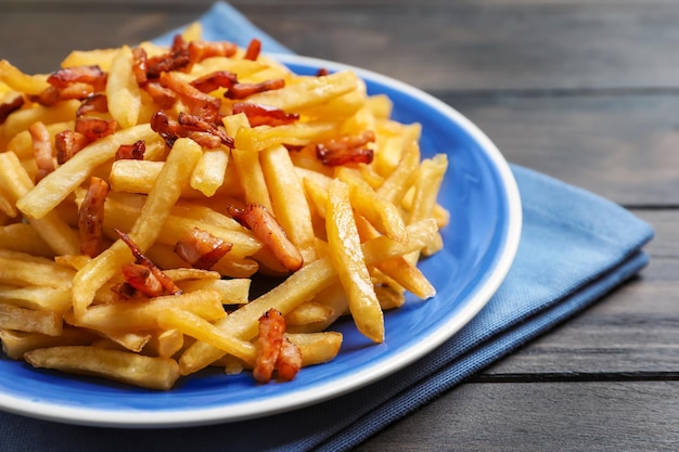 Plato con papas fritas y tocino en mesa de madera