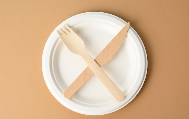 Plato de papel blanco vacío y cuchillo y tenedor de madera, objetos cruzados, vista superior