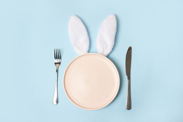 Plato de Pascua vacío rosa con orejas de conejo sobre fondo azul.