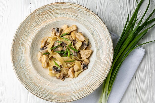 Un plato de pasta de champiñones con cebollas verdes sobre una mesa blanca