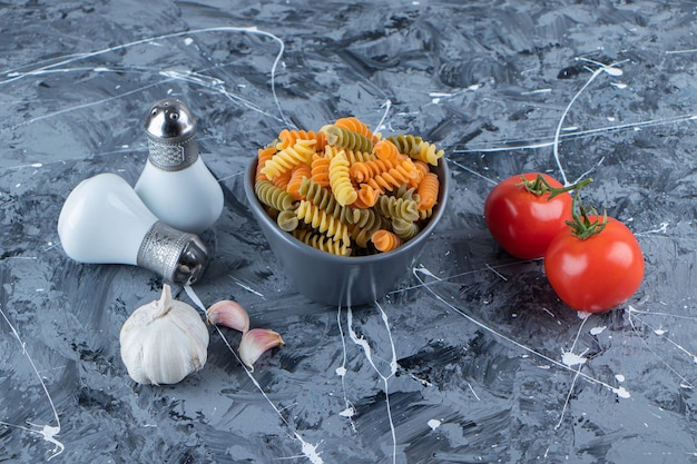 Un plato de pasta cruda con verduras frescas y especias sobre una superficie de mármol.