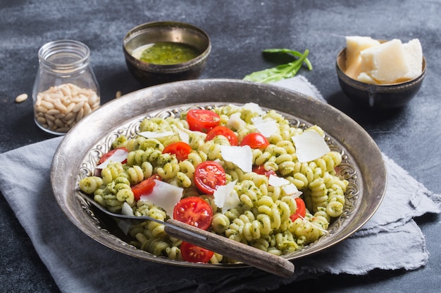 Plato de pasta fusilli con salsa de pesto, tomates cherry sobre fondo oscuro