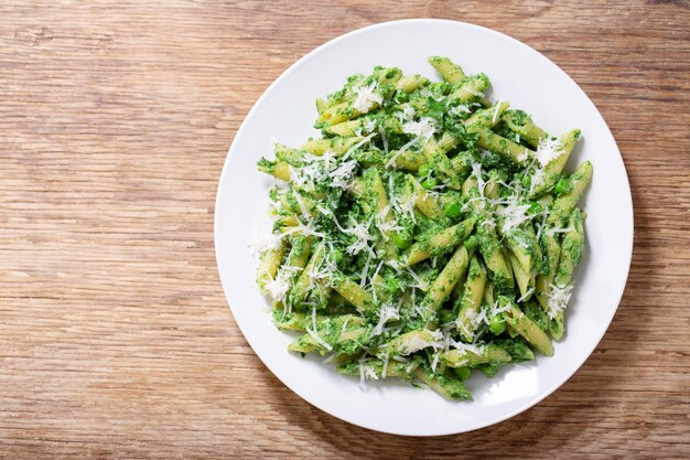 Plato de pasta con guisantes de espinaca y queso parmesano sobre un fondo de madera.