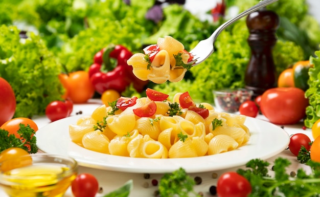 Plato de pasta italiana cocida, tubo rigate en horquilla con tomates y hojas de albahaca