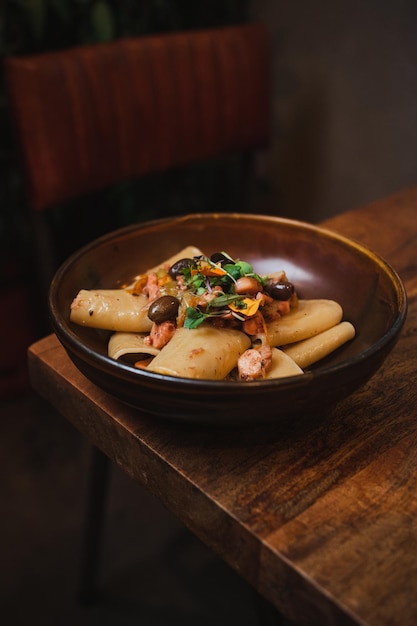 Plato de pasta de paccheri, pulpo, tomates de cereza y aceitunas en un restaurante italiano