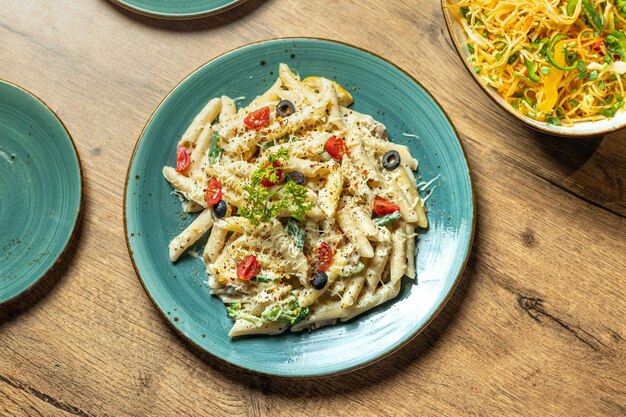 Un plato de pasta con pollo, aceitunas y queso sobre una mesa.