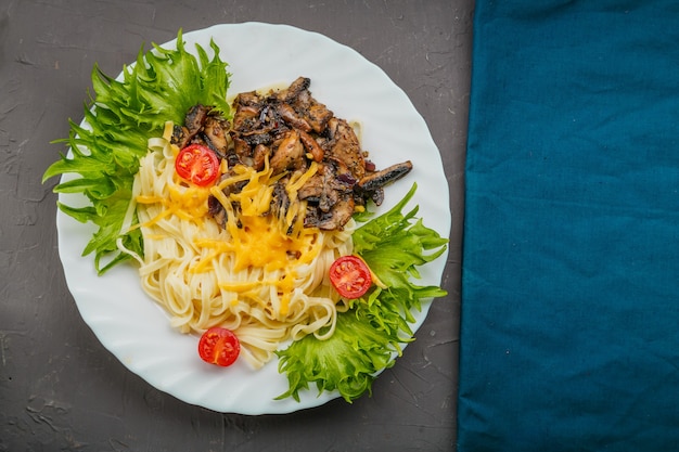 Un plato de pasta con queso y champiñones decorado con hierbas sobre un fondo gris junto a una servilleta azul. Copie el espacio. Foto horizontal