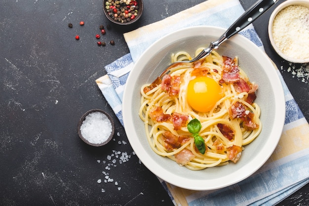 Plato de pasta tradicional italiana, espaguetis a la carbonara con yema, queso parmesano, tocino en placa sobre fondo de piedra rústica negra