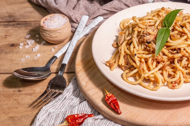 Plato de pasta tradicional siciliana de berenjena salteada con salsa de tomate. Comida servida en un plato de cerámica, cocina italiana, luz dura moderna, sombra oscura. Fondo de mesa de madera, cerrar