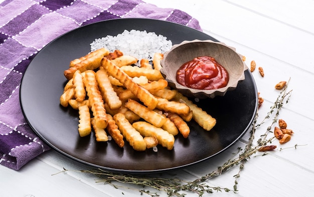 Plato de patatas francesas caseras con ketchup y sal marina en servilleta a cuadros y backgro de madera blanca