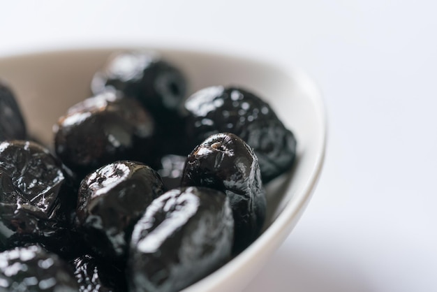 Plato pequeño con dátiles negros sobre un fondo blanco.