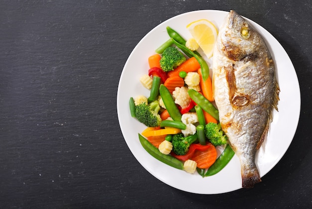 Plato de pescado al horno con verduras sobre fondo oscuro, vista superior