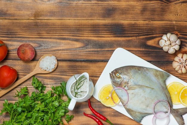 Plato de pescado cocinado con varios ingredientes. Pescado crudo fresco decorado con rodajas de limón y hierbas sobre mesa de madera.