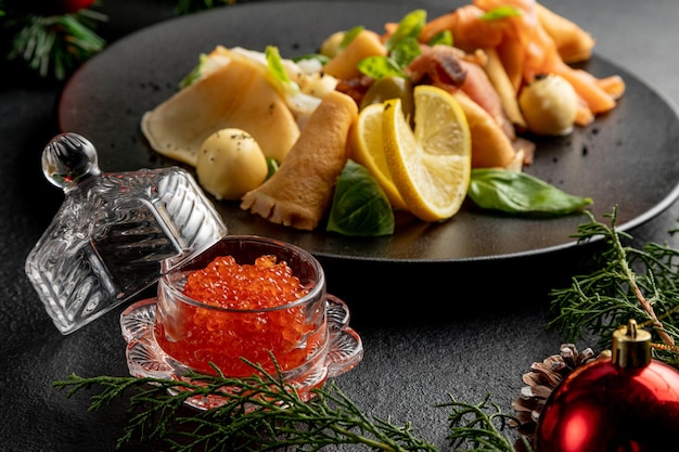 Plato de pescado en un plato negro con caviar rojo sobre un fondo oscuro de Navidad con juguetes de Navidad y ramas de abeto