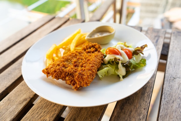 Plato de pescado rebozado con papas fritas. Pescado en un plato con patatas y ensalada en un café de verano.