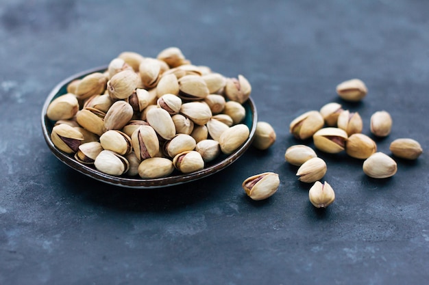 Un plato con pistachos crudos en una concha sobre un fondo gris oscuro