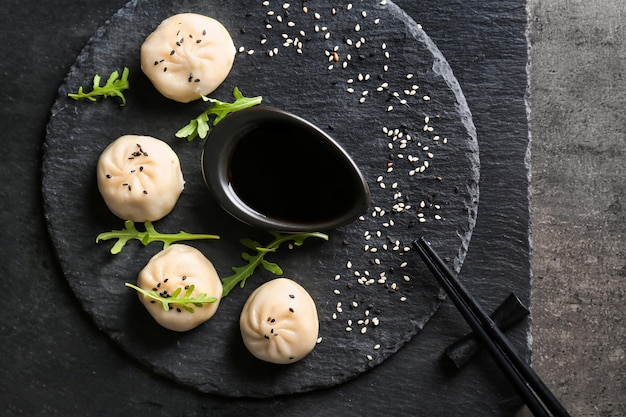 Plato de pizarra con sabrosas albóndigas baozi y salsa de soja en la mesa