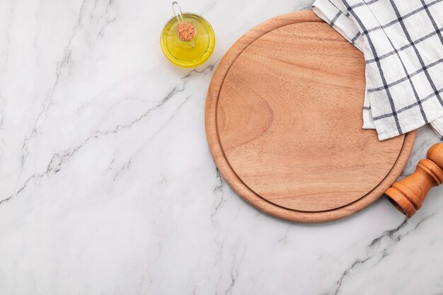 Plato de pizza de madera vacía con servilleta en la mesa de la cocina de piedra de mármol. Tablero de pizza y mantel sobre fondo de mármol blanco.