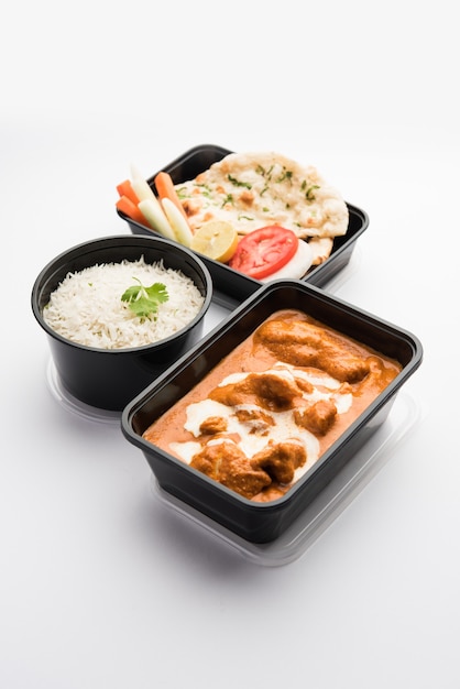 Plato de pollo al curry con mantequilla india servido en un recipiente de plástico negro para la entrega de alimentos a casa
