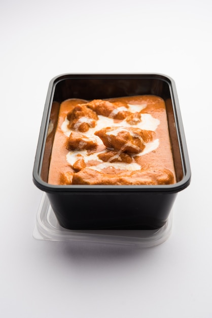Plato de pollo al curry con mantequilla india servido en un recipiente de plástico negro para la entrega de alimentos a casa
