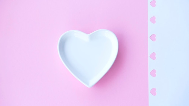 Plato de porcelana blanca en forma de corazón sobre fondo rosa