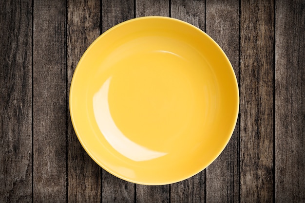 Plato de porcelana circular amarillo simple sobre madera con trazado de recorte