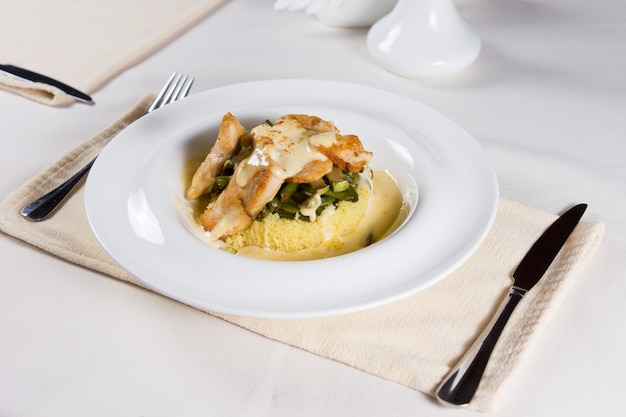 Foto plato preparado servido en un tazón blanco, colocado en un lugar con tenedor y cuchillo en la mesa del restaurante