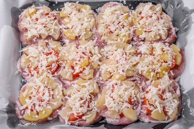 Un plato que consiste en carne, tomates, piña, queso, especias y hierbas sobre pergamino en una bandeja para hornear. Preparación de alimentos para hornear en el horno.