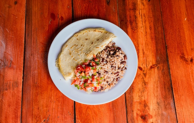 Plato de quesillo con gallo pinto y pico de gallo sobre mesa de madera Comida nicaragüense Gallo pinto con pico de gallo y Quesillo servido