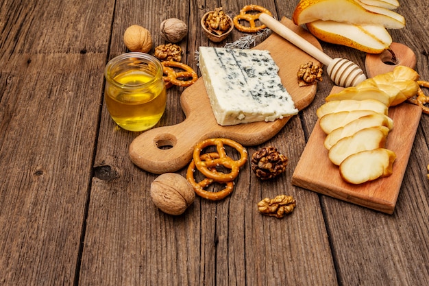 Plato de queso antipasti con queso ahumado y azul, galletas, miel, nueces y pera madura. Receta de merienda tradicional
