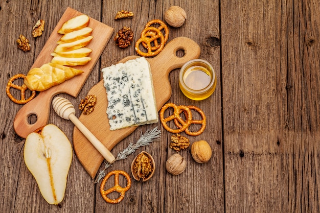 Plato de queso antipasti con queso ahumado y azul, galletas, miel, nueces y pera madura. Receta de merienda tradicional