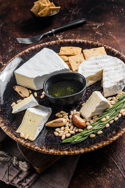 Plato de queso con brie y camembert sobre plato rústico con nueces y miel. fondo oscuro Vista superior.