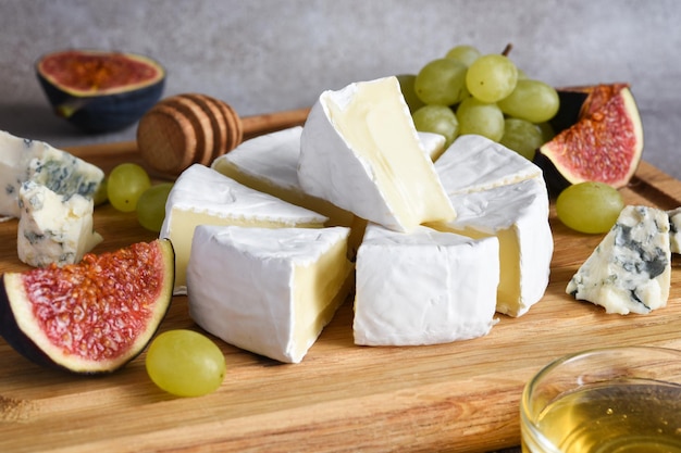 Plato de queso camembert y queso azul con uvas, higos, miel sobre una tabla de madera. Bandeja de queso