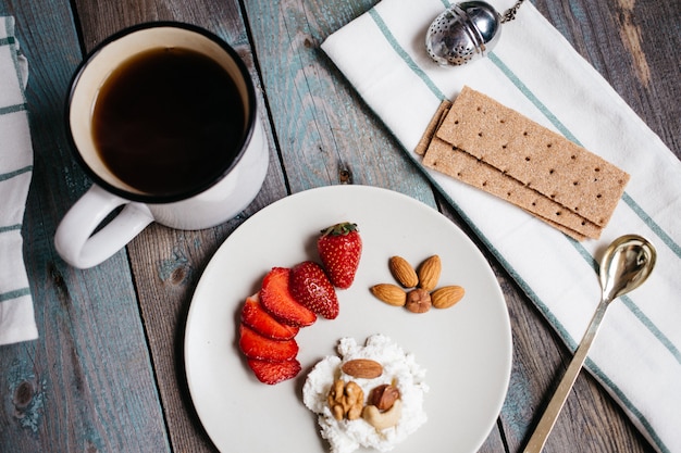 Plato con queso cottage, fresas y nueces, una taza de café y toallas en la mesa de madera, comida saludable, desayuno